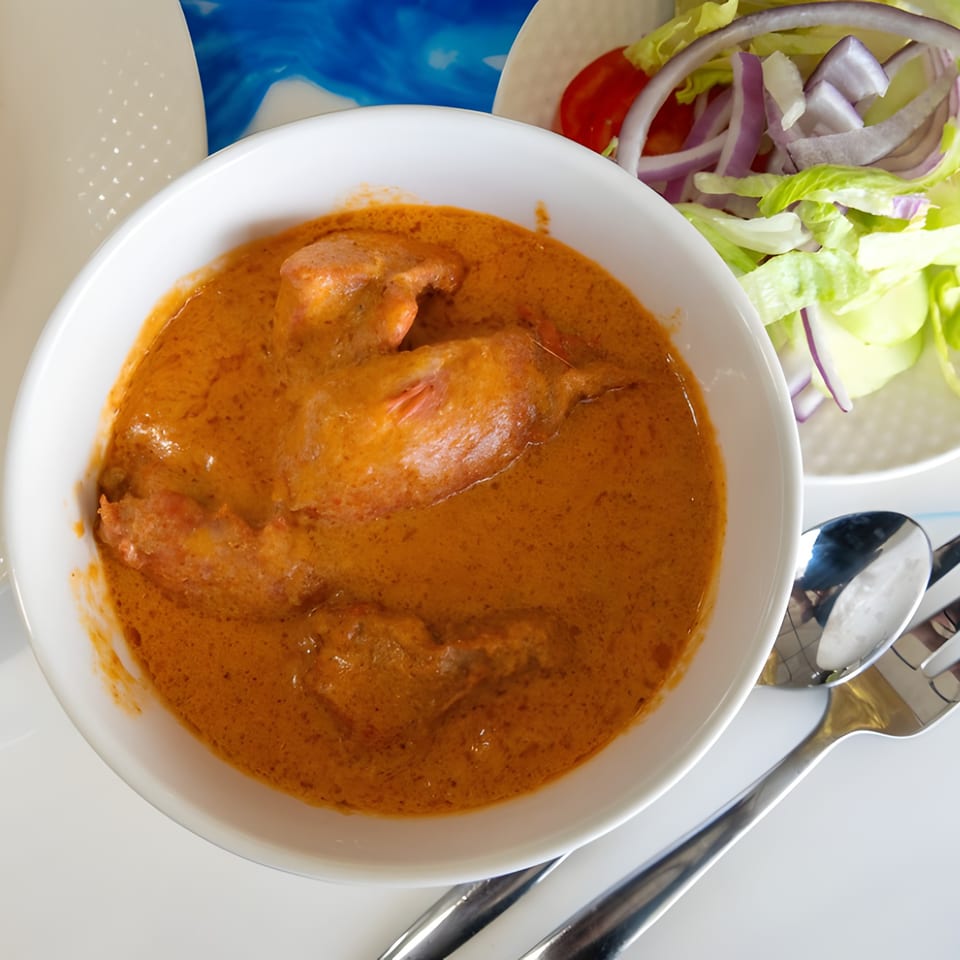 A white bowl of chicken tikka masala with a side salad and silverware.
