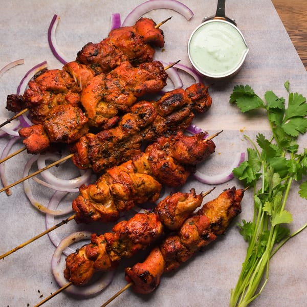Grilled chicken tikka skewers with red onion, cilantro, and a side of green dipping sauce.