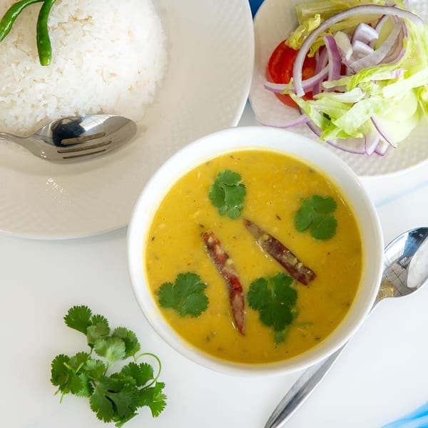 A bowl of yellow lentil soup with cilantro and chilies, served with rice and salad.