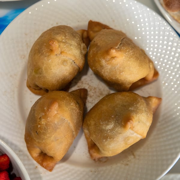 Four golden-brown empanadas, lightly dusted with spices, arranged on a white textured plate.