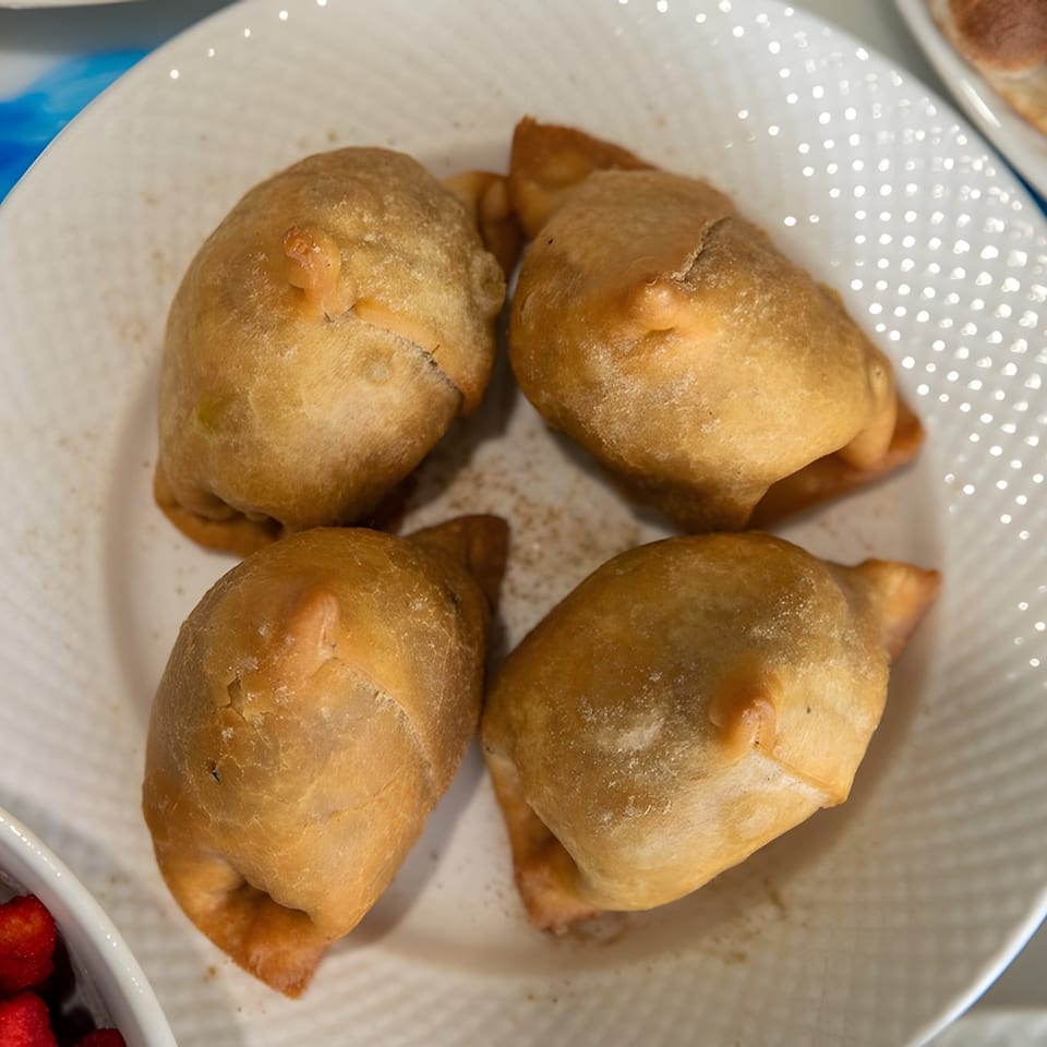 Four golden-brown empanadas, lightly dusted with spices, arranged on a white textured plate.