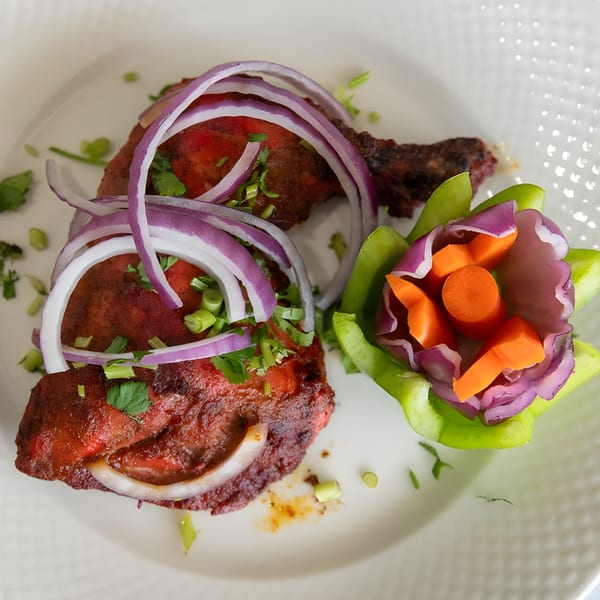 Tandoori chicken with red onion, cilantro, and a bell pepper garnish on a white plate.