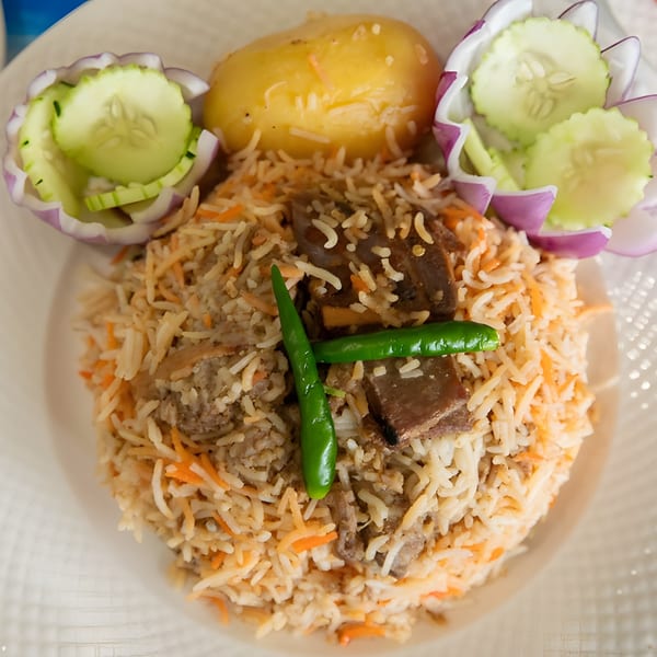 Biryani with meat, rice, green chilies, a potato, and cucumber-onion salad on a white plate.
